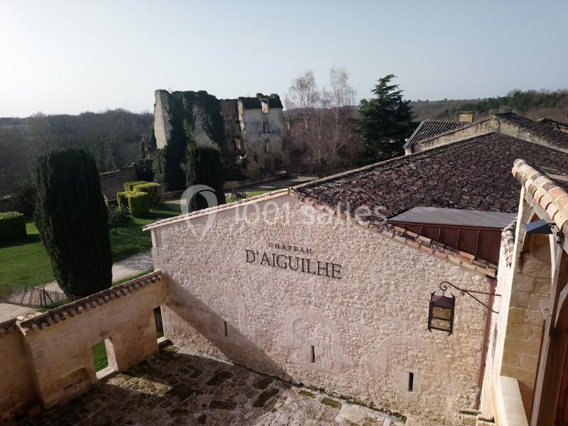 Vue sur la façade en pierre du Château d'Aiguilhe avec des ruines et un jardin arboré en arrière-plan.