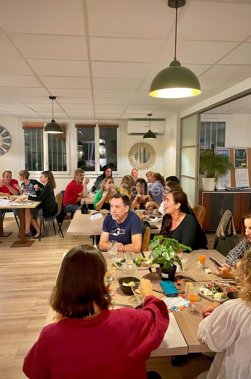 Des personnes assises autour de tables dans une salle lumineuse, partageant un repas ou discutant.