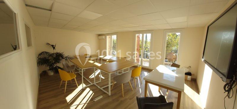 Salle de réunion lumineuse avec table en bois, chaises colorées, plantes et grandes fenêtres donnant sur un espace extérieur.