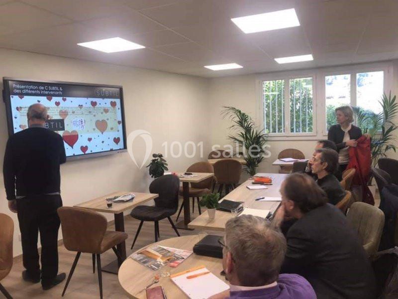 Un groupe de personnes assiste à une présentation sur un écran dans une salle de réunion lumineuse.