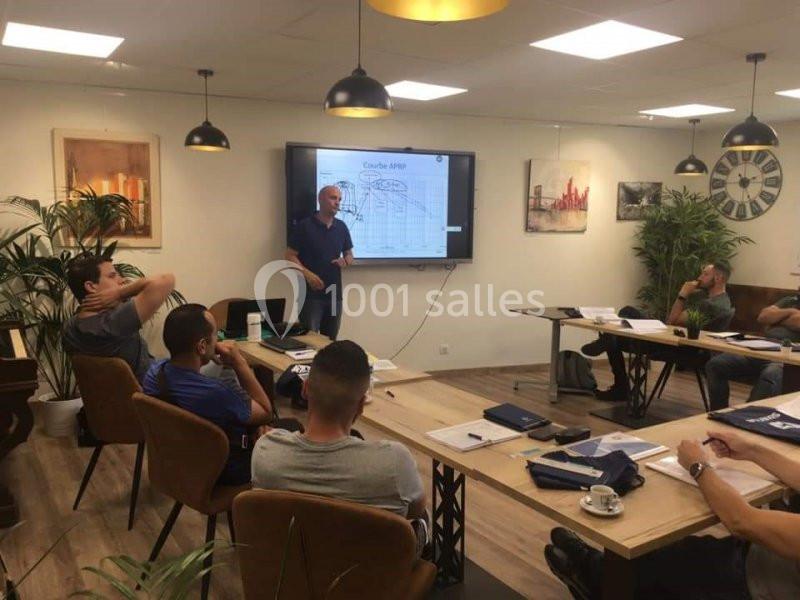 Un homme donne une présentation devant un écran dans une salle de réunion avec plusieurs participants assis.