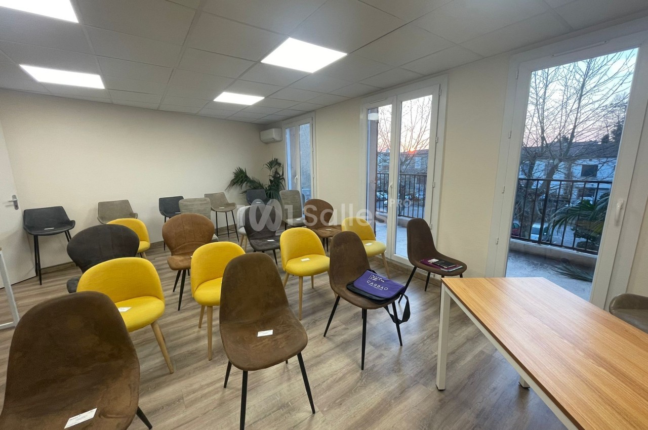 Salle de réunion lumineuse avec des chaises jaunes et marron disposées face à une table, fenêtres donnant sur l'extérieur.