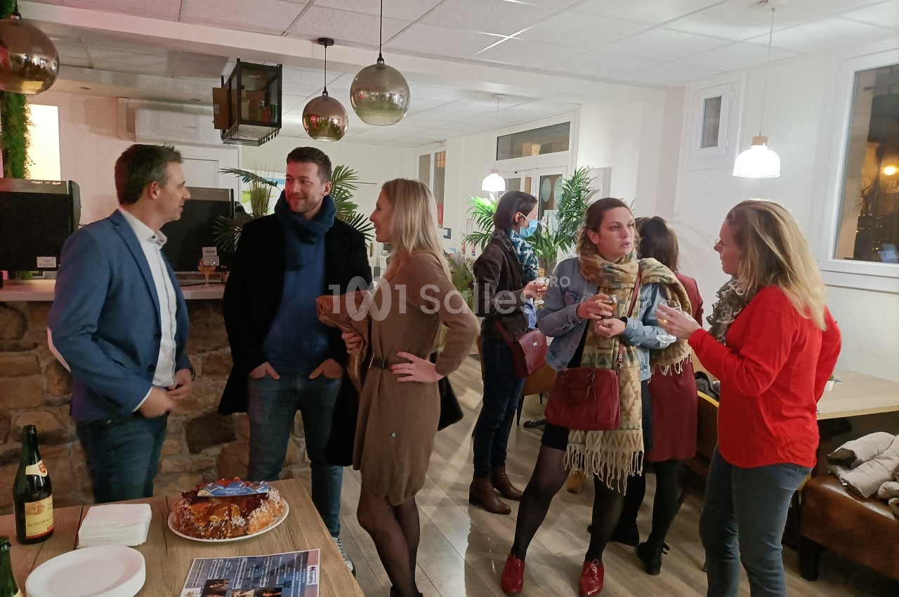 Un groupe de personnes discute dans un espace intérieur convivial avec des tables et des décorations lumineuses.