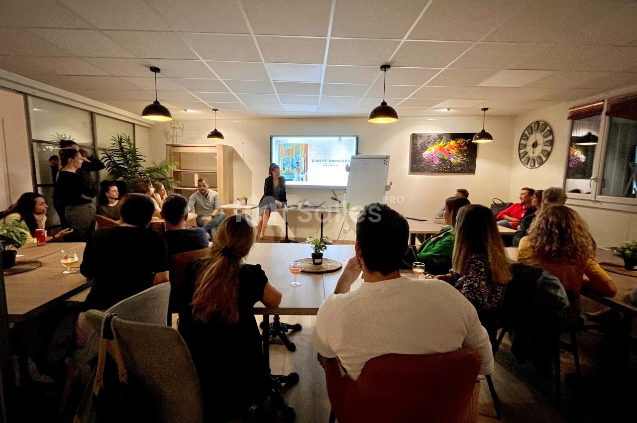 Groupe de personnes assises dans une salle, écoutant une présentation projetée sur un écran.