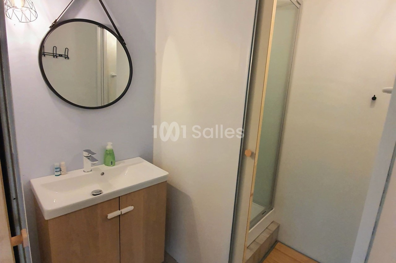 Salle de bain avec lavabo sur meuble en bois, miroir rond mural, et douche avec porte coulissante.
