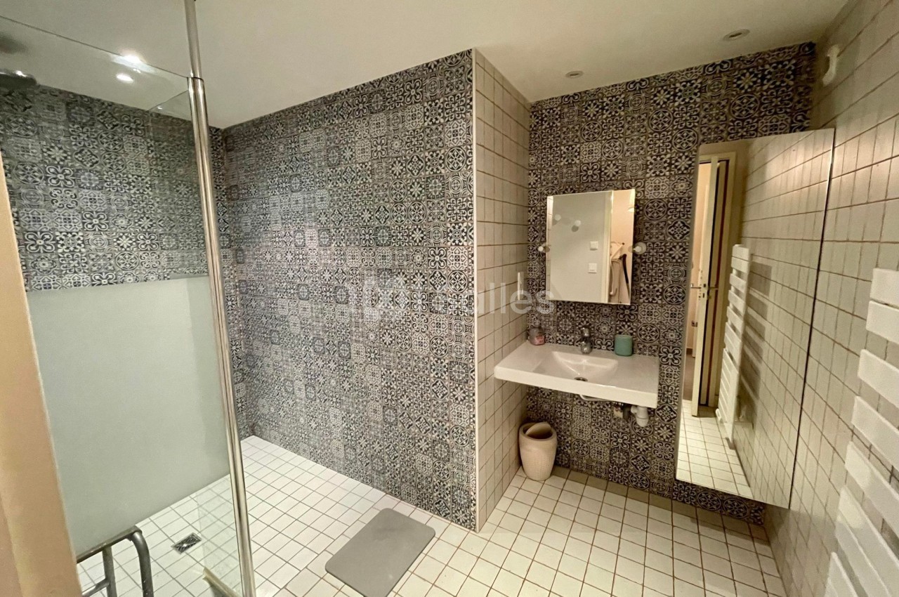 Salle de bain avec douche à l'italienne, murs en carreaux à motifs, lavabo suspendu et miroir éclairé.