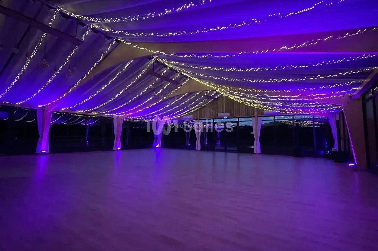 Salle spacieuse avec un plafond décoré de guirlandes lumineuses violettes et un sol en bois clair.