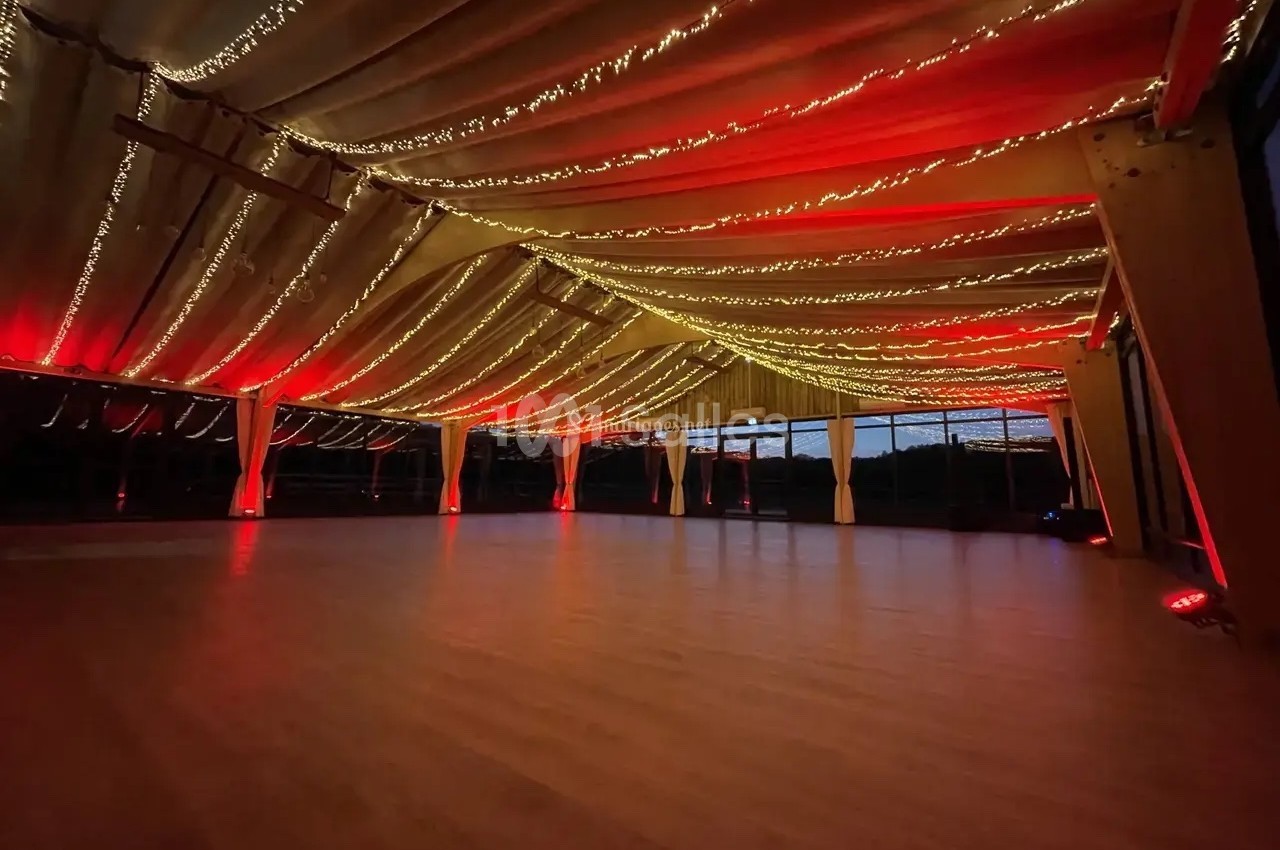 Plafond décoré de guirlandes lumineuses rouges et dorées dans une grande salle vide avec un sol en bois.
