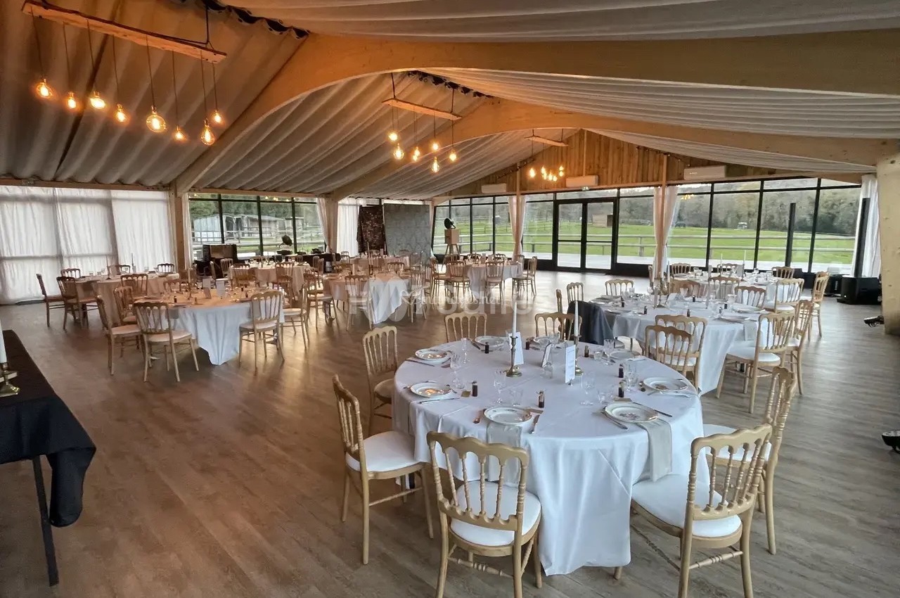 Salle de réception lumineuse avec tables rondes dressées, chaises en bois clair et grandes baies vitrées donnant sur l…