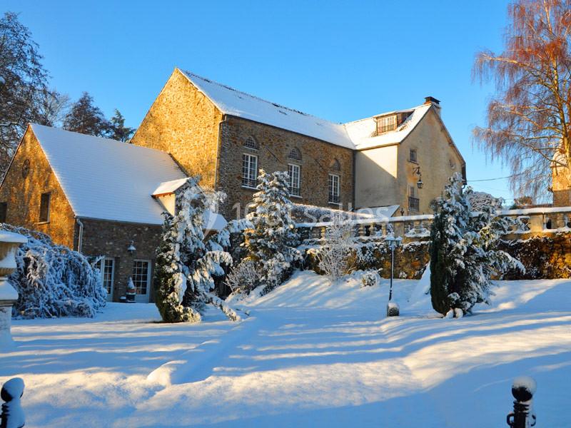 Bâtiment en pierre entouré d'arbres et de neige sous un ciel bleu ensoleillé.