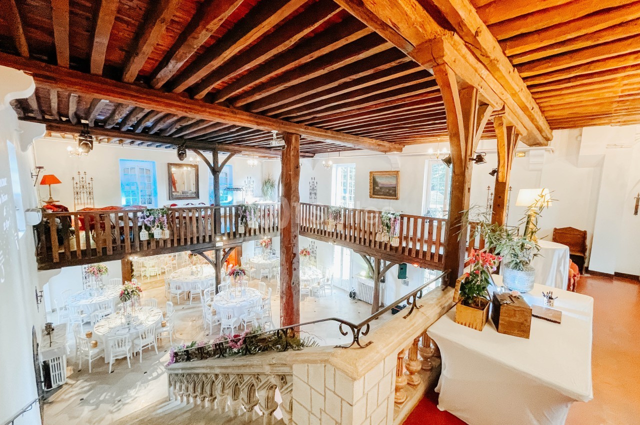 Salle lumineuse avec mezzanine en bois, tables dressées pour un événement et décoration florale élégante.