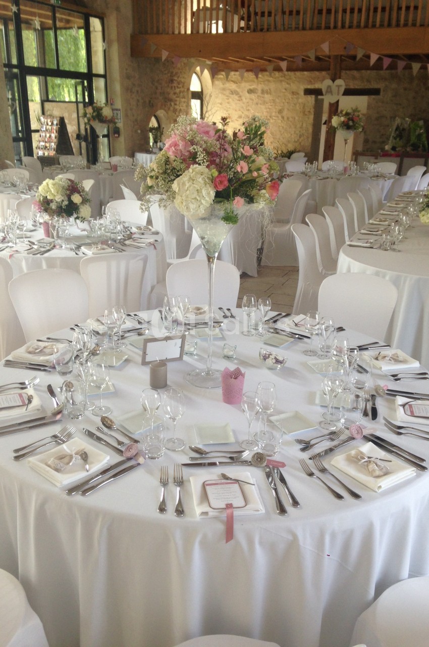 Salle de réception décorée pour un mariage avec tables rondes dressées, nappes blanches et compositions florales.