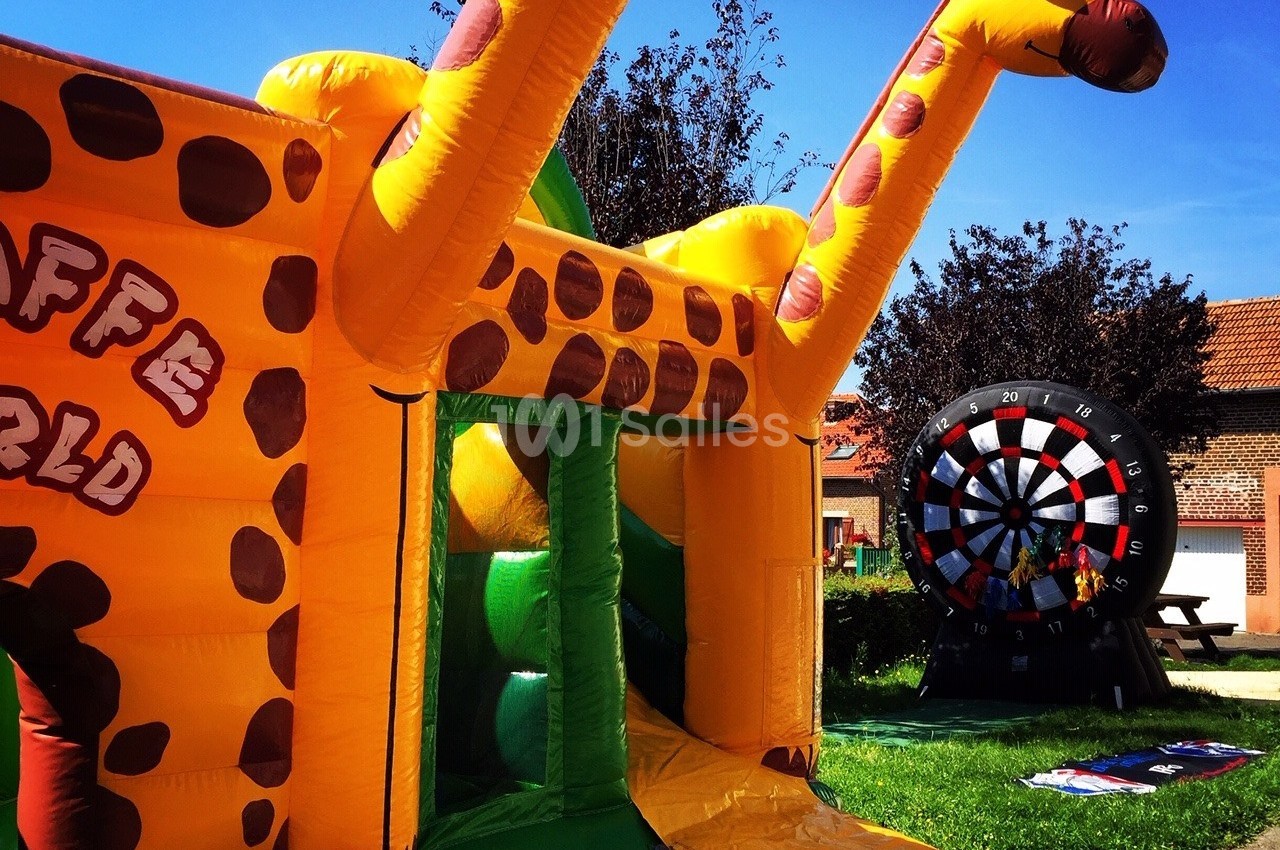 Structure gonflable en forme de girafe dans un espace extérieur ensoleillé, avec une cible géante en arrière-plan.