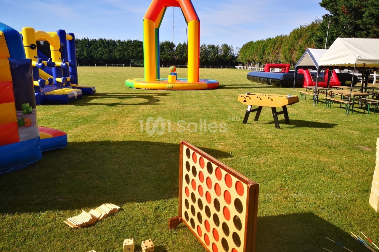Jeux en plein air sur une pelouse, incluant structures gonflables, puissance 4 géant et baby-foot.