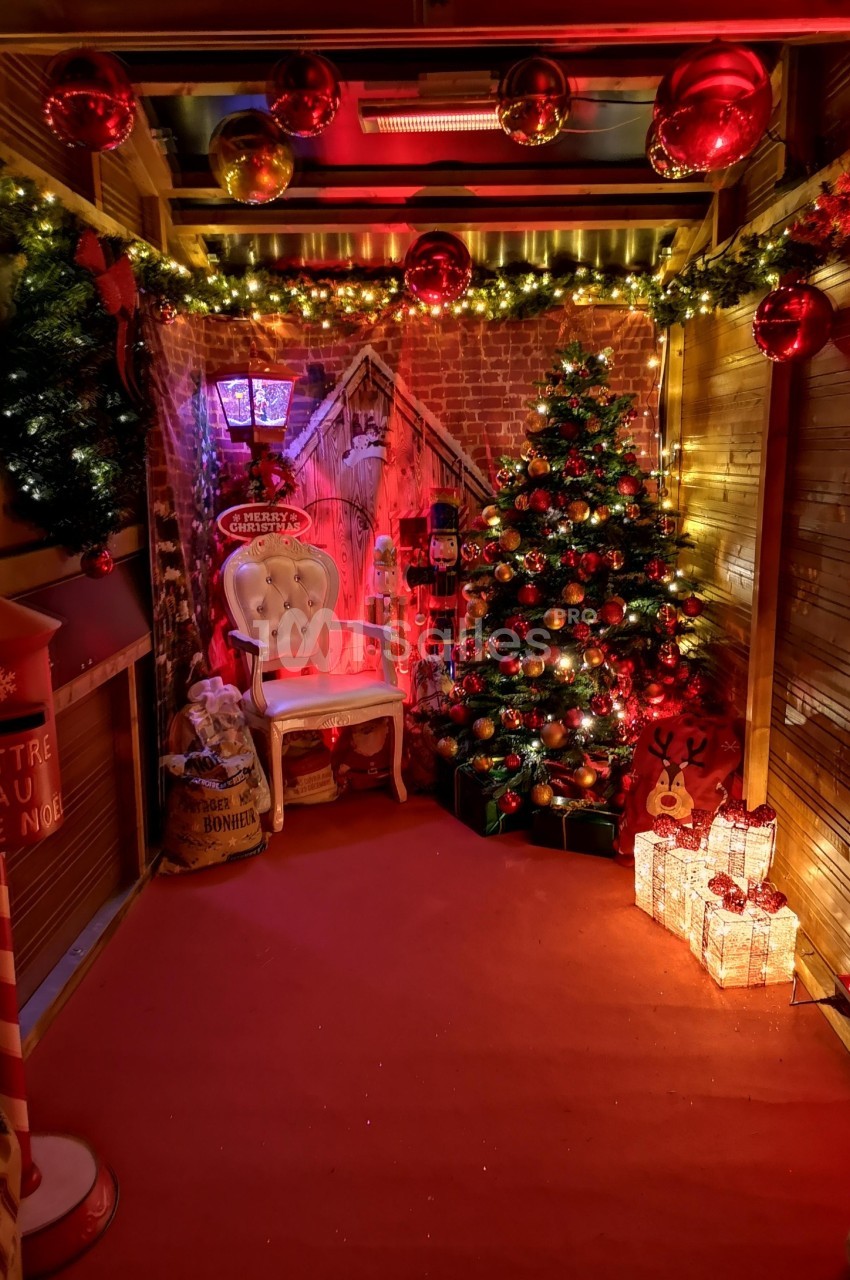 Décoration de Noël avec sapin illuminé, guirlandes, cadeaux, fauteuil blanc et boîte aux lettres festive.