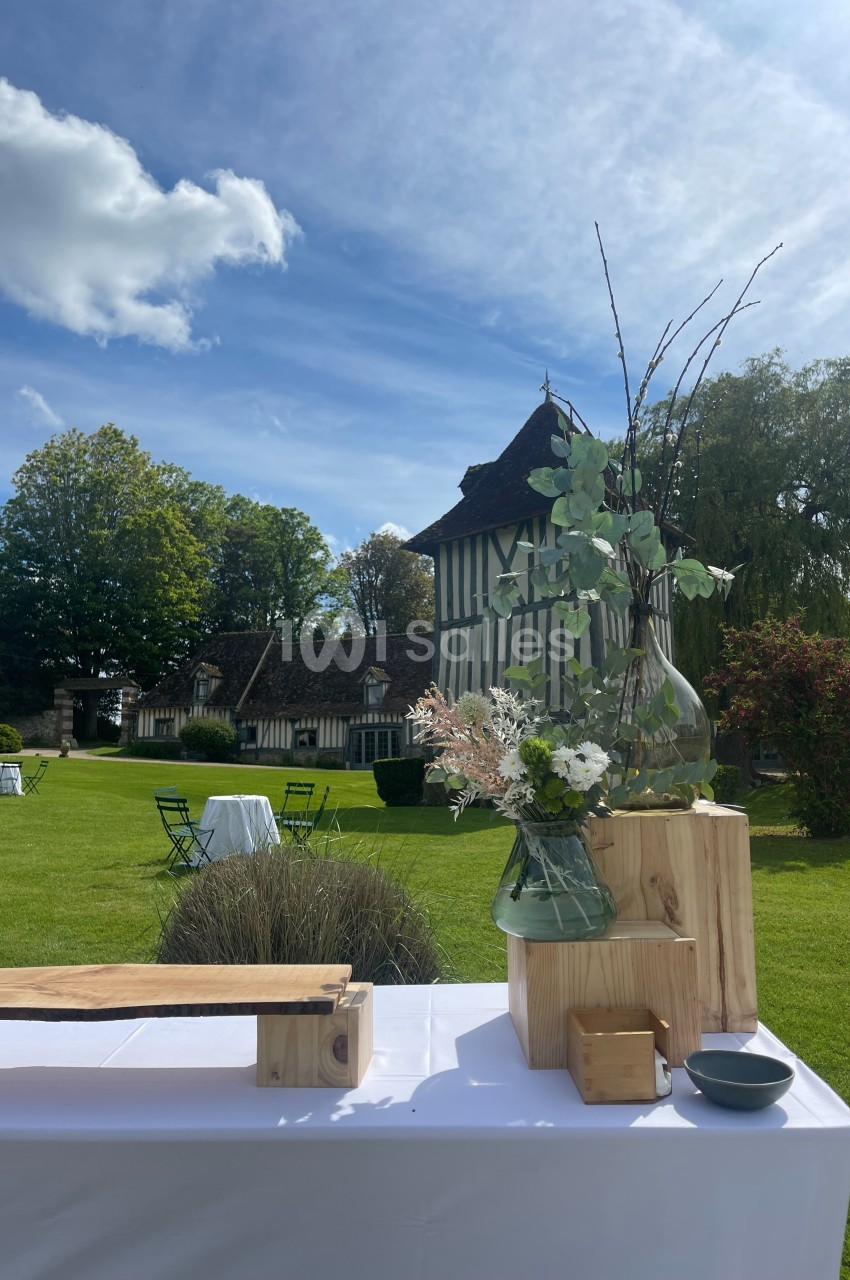 Table décorée avec des fleurs et des éléments en bois, installée dans un jardin devant une maison à colombages.