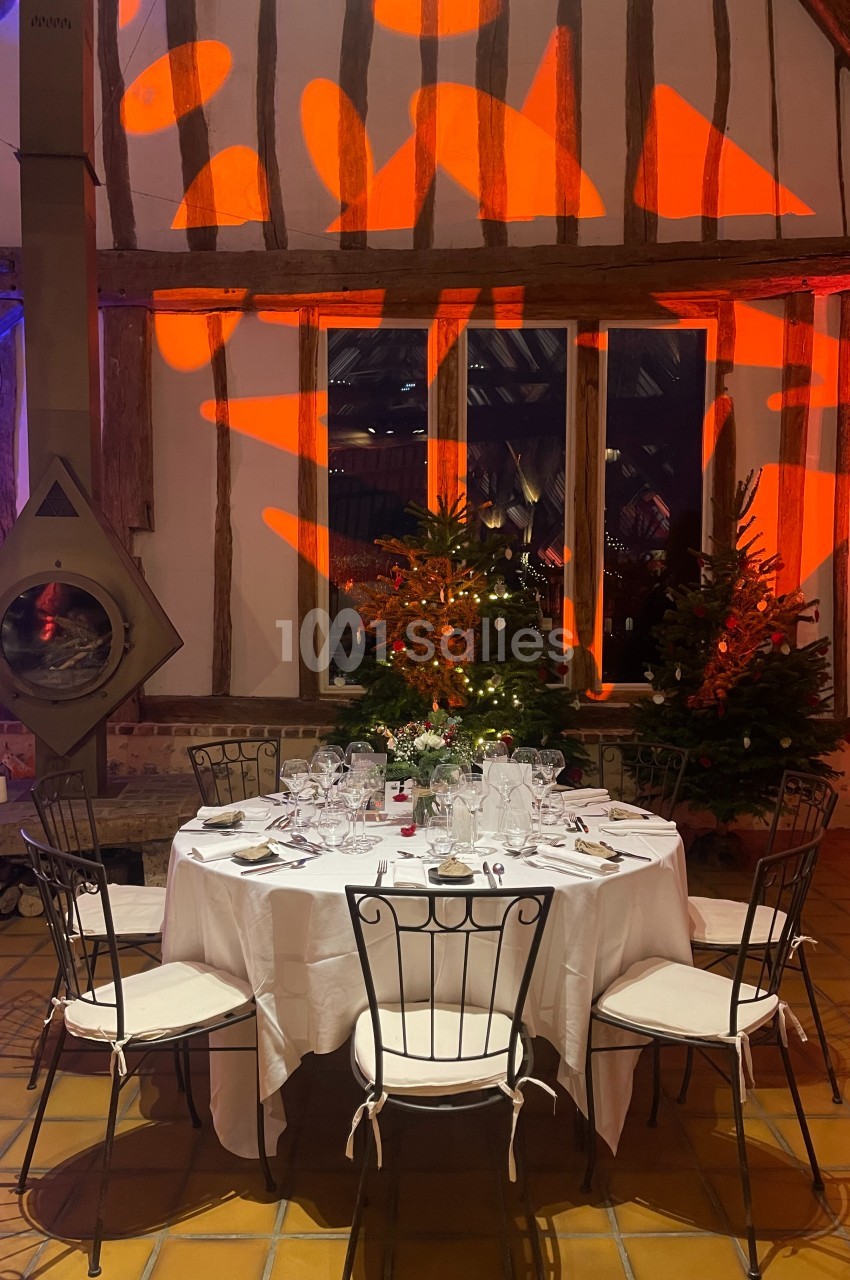 Table ronde dressée avec vaisselle élégante, entourée de chaises en métal, dans une salle rustique décorée de lumières et…
