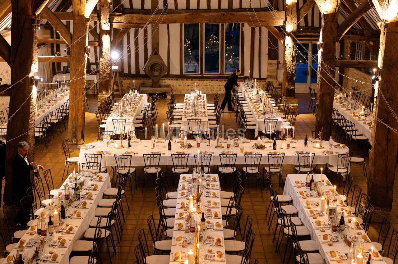 Grande salle de réception avec de longues tables dressées, décorée de lumières suspendues et d'éléments rustiques.