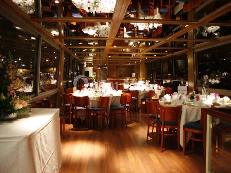 Salle de réception élégante avec tables rondes dressées, chaises en bois et éclairage chaleureux.