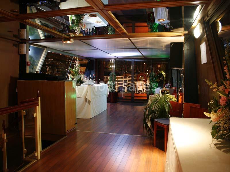 Intérieur d'une salle de réception avec parquet, tables dressées, décorations florales et éclairage chaleureux.