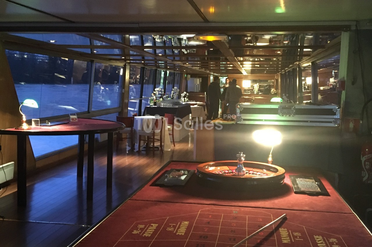 Salle de réception sur un bateau avec une table de roulette au premier plan et des tables dressées en arrière-plan.