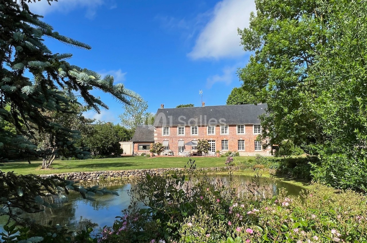 Grande maison en briques rouges entourée d'un jardin verdoyant avec un étang au premier plan.