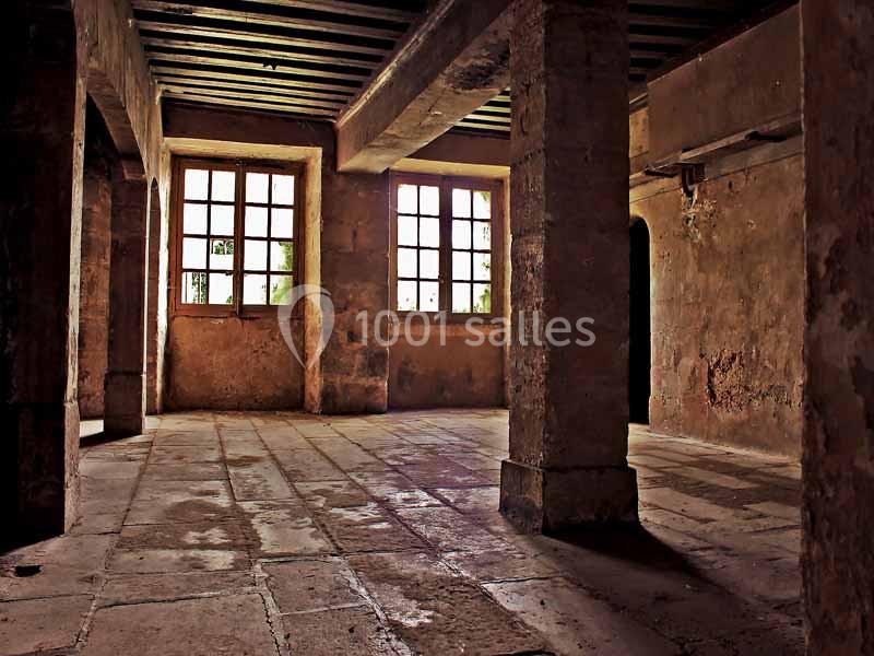 Intérieur d'une pièce ancienne avec des colonnes en pierre, un sol carrelé et des fenêtres laissant entrer la lumière.
