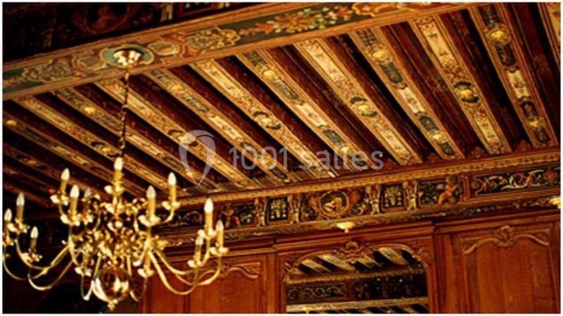 Plafond en bois sculpté et peint avec des motifs décoratifs, accompagné d'un lustre doré suspendu.