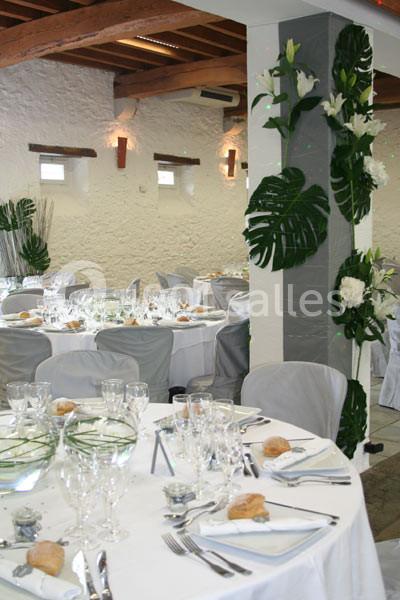 Salle de réception avec tables rondes dressées, nappes blanches, vaisselle élégante et décoration florale.