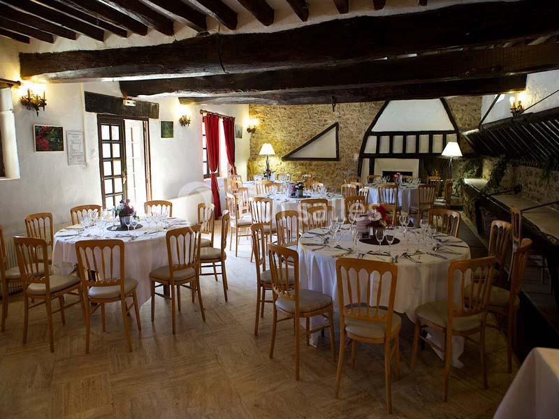 Salle de réception rustique avec poutres apparentes, tables rondes dressées et chaises en bois clair.