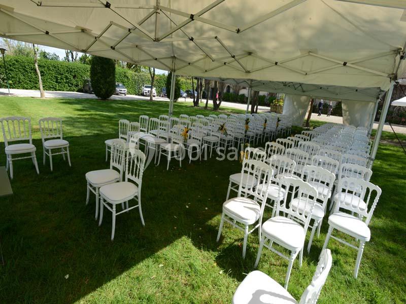 Chaises blanches alignées sous une tente dans un espace extérieur verdoyant, préparées pour un événement.