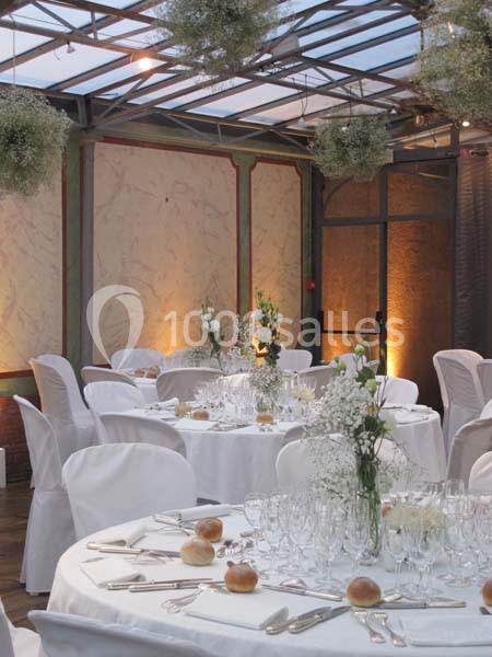 Salle de réception élégante avec tables rondes dressées, nappes blanches et décorations florales suspendues.