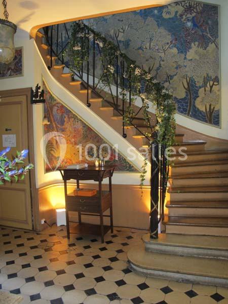 Escalier en bois avec rampe décorée de feuillage, entouré de fresques murales colorées et éclairage chaleureux.