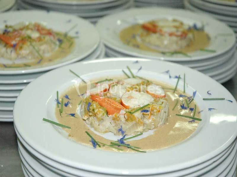 Assiette de risotto garni de crevettes, légumes et fleurs comestibles, servie avec une sauce crémeuse.