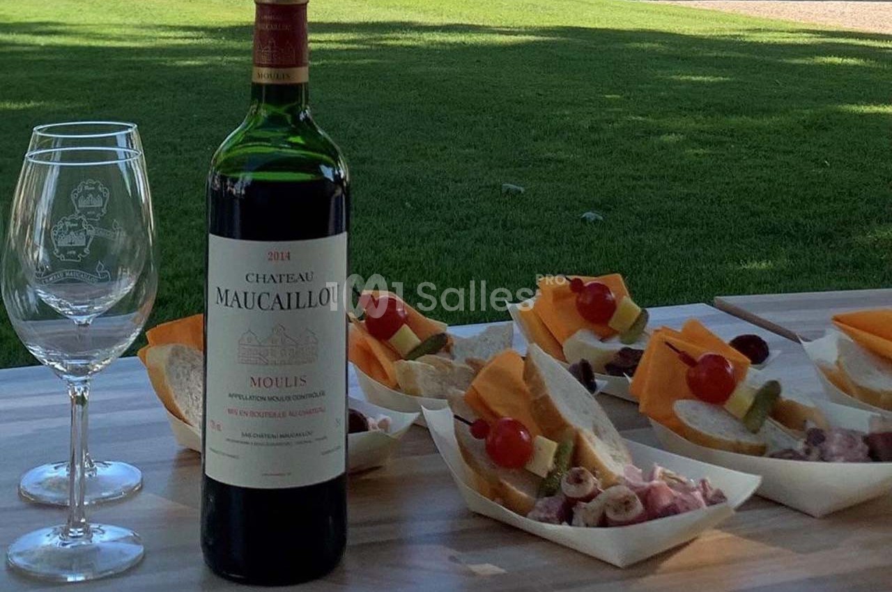 Bouteille de vin rouge avec deux verres et des plateaux de charcuterie et fromage sur une table en extérieur.