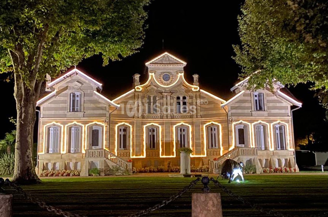 Façade d'un bâtiment illuminé la nuit, entouré d'arbres et d'une pelouse bien entretenue.