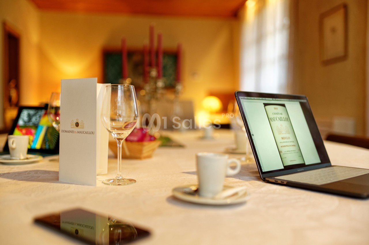 Table dressée avec des verres, tasses à café, un ordinateur portable affichant une page, et un menu debout.