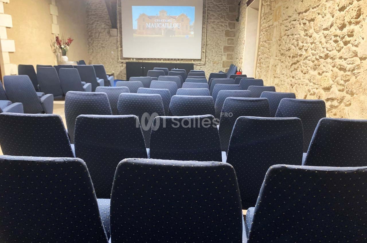 Salle de conférence avec des rangées de sièges bleus et un écran de projection affichant une image.