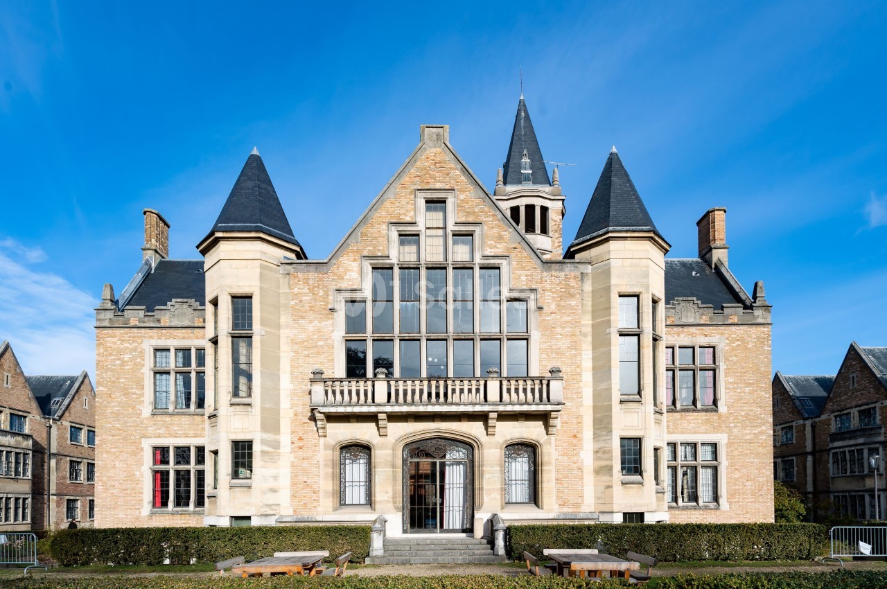 Façade d'un bâtiment en pierre de style néogothique avec grandes fenêtres et tours, sous un ciel bleu dégagé.