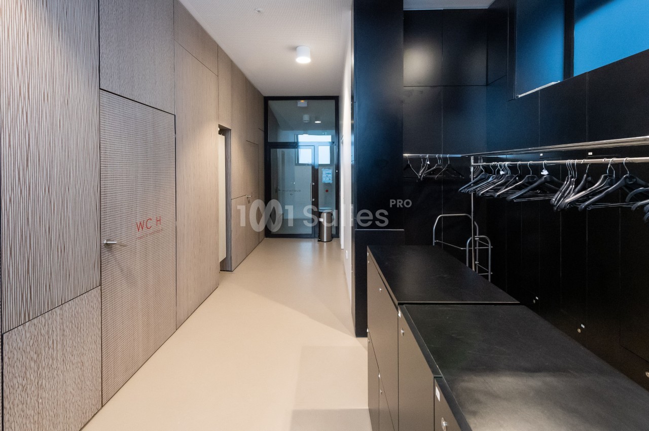 Vestiaire moderne avec casiers noirs, porte marquée ’WC’ à gauche et cintres suspendus sur une tringle métallique.