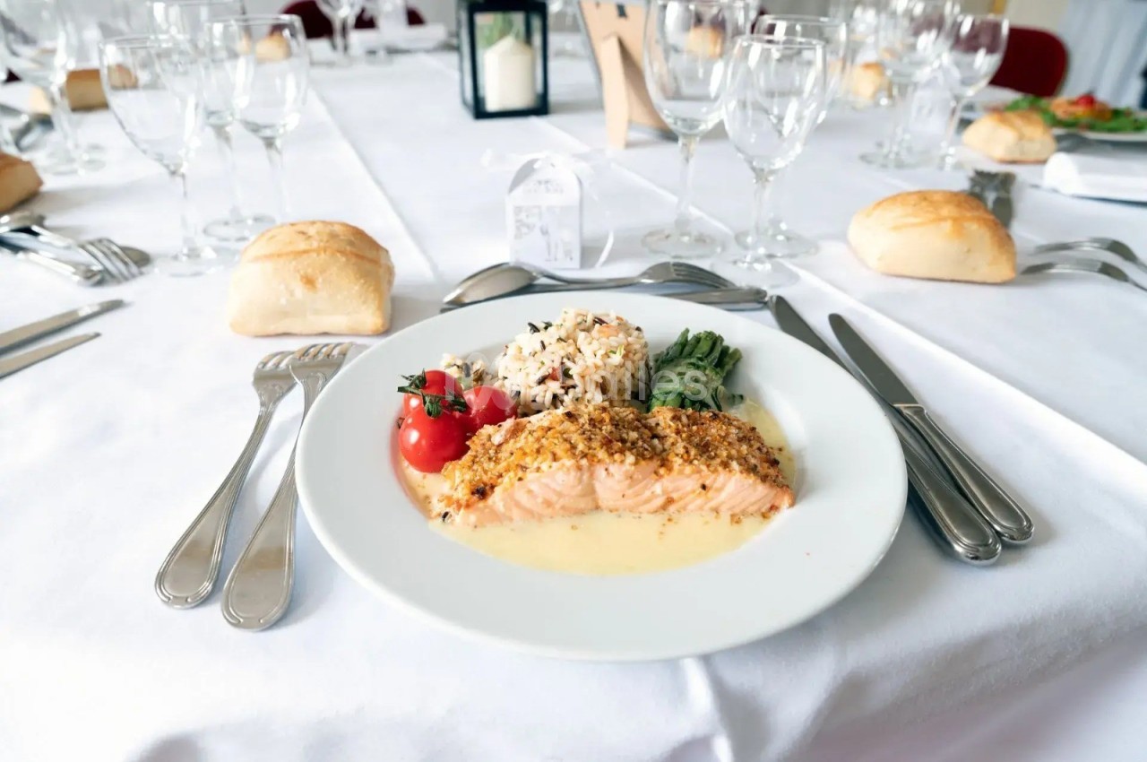 Assiette de saumon en sauce avec riz, légumes et tomates cerises, servie sur une table dressée avec couverts et verres.