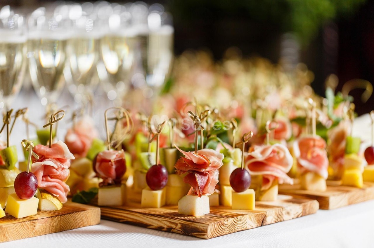 Plateaux de bouchées apéritives avec fromage, raisin, jambon et brochettes, accompagnés de verres de champagne en arrière…