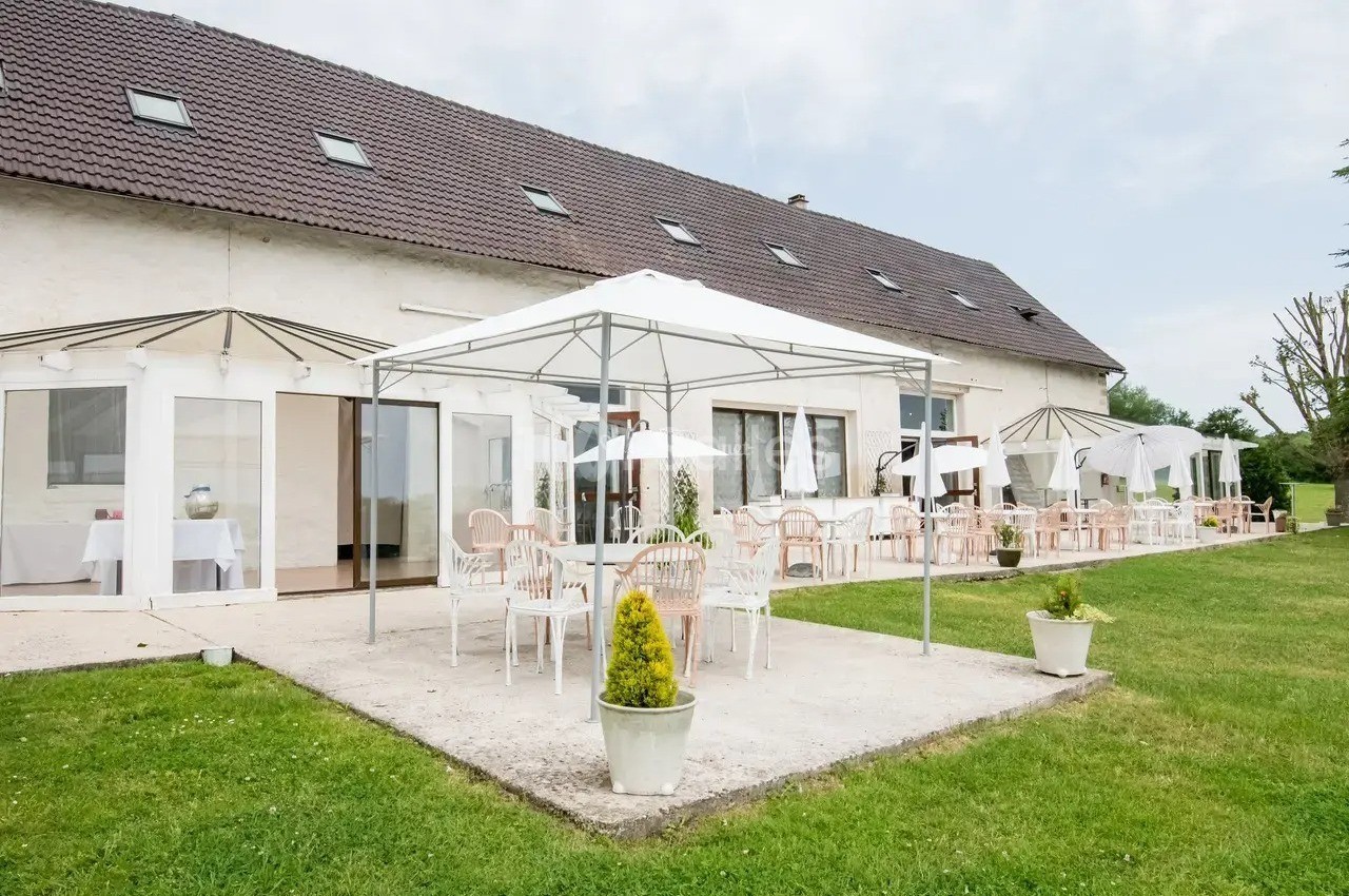 Terrasse extérieure avec tables et chaises sous des tonnelles blanches, devant un grand bâtiment à toit en pente.