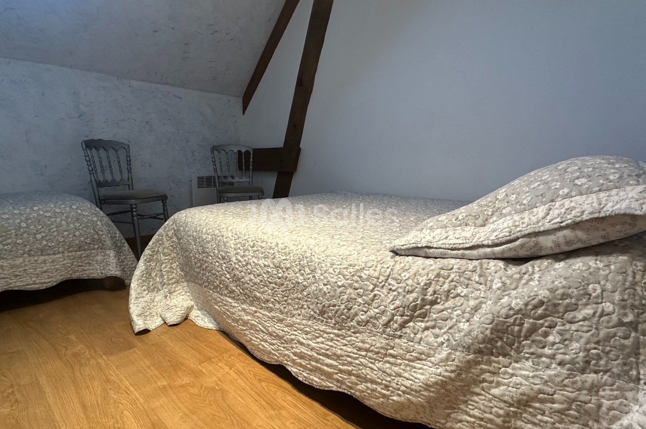 Deux lits simples avec couvre-lits texturés dans une chambre mansardée au sol en bois et murs clairs.