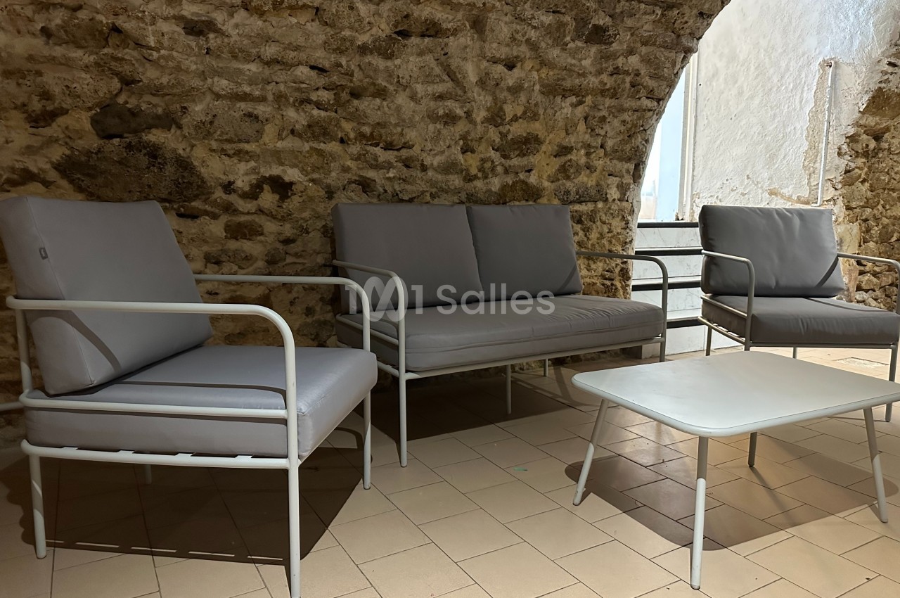 Mobilier de salon gris clair avec structure métallique, installé dans une pièce aux murs en pierre apparente.