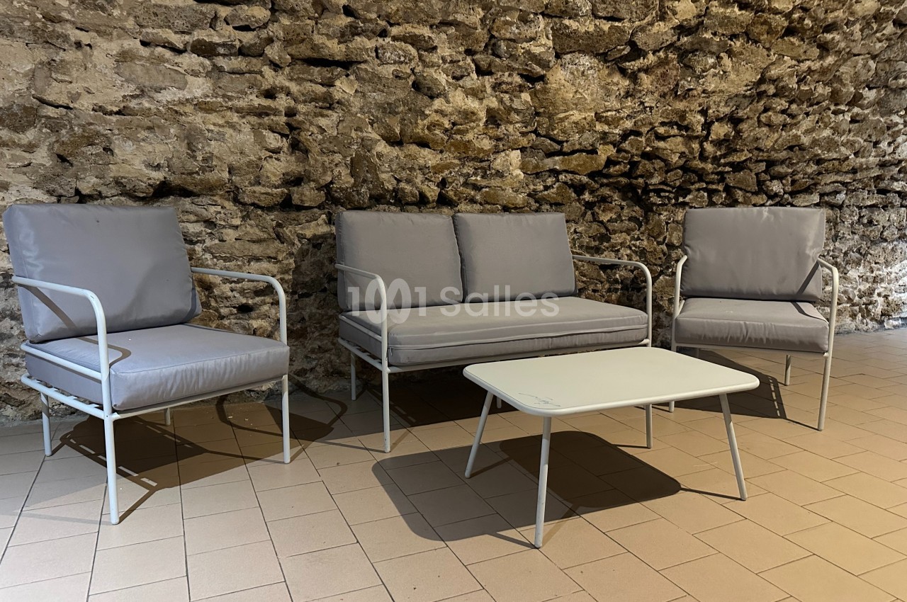 Mobilier de salon de jardin avec deux fauteuils, un canapé et une table basse, disposés sur un sol carrelé devant un mur en…