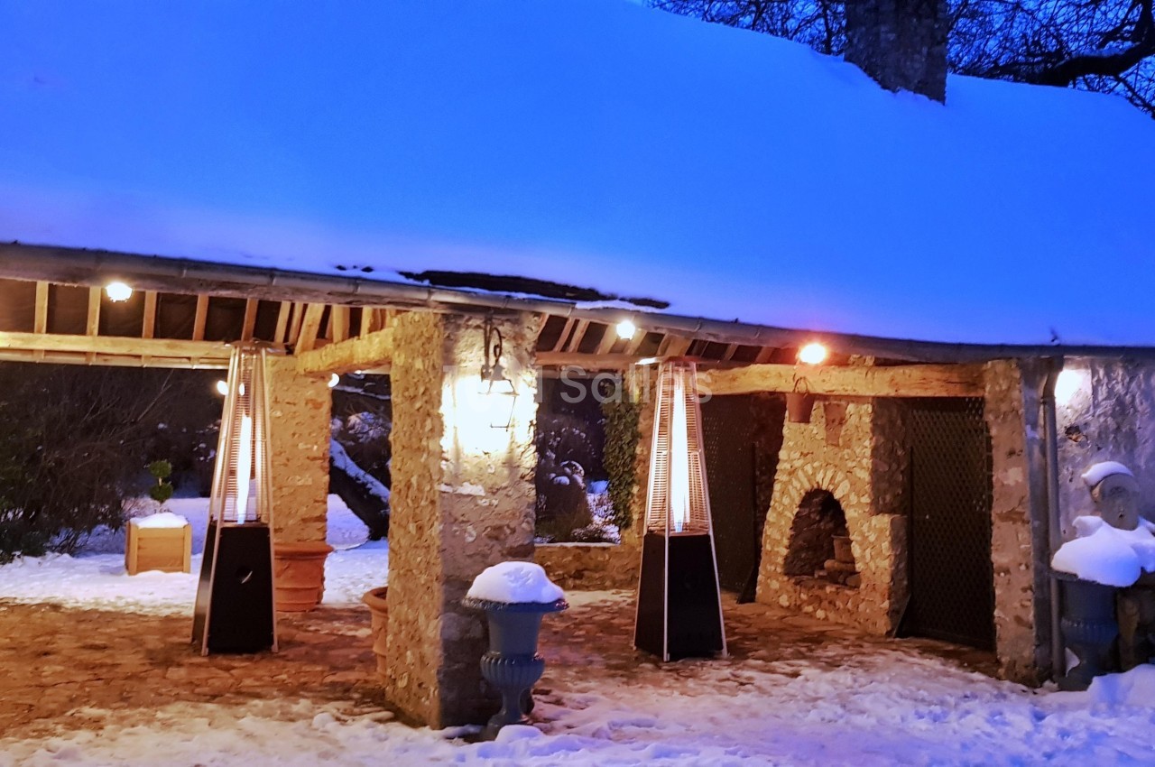 Abri en pierre éclairé, avec des chauffages extérieurs et un toit enneigé, entouré d'un paysage hivernal.