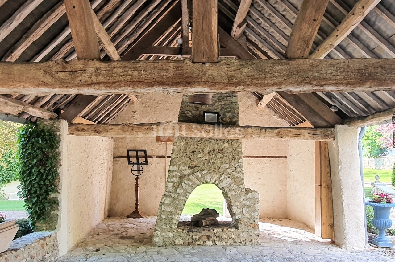 Abri en pierre et bois avec cheminée ouverte, entouré de verdure et éclairé par la lumière naturelle.