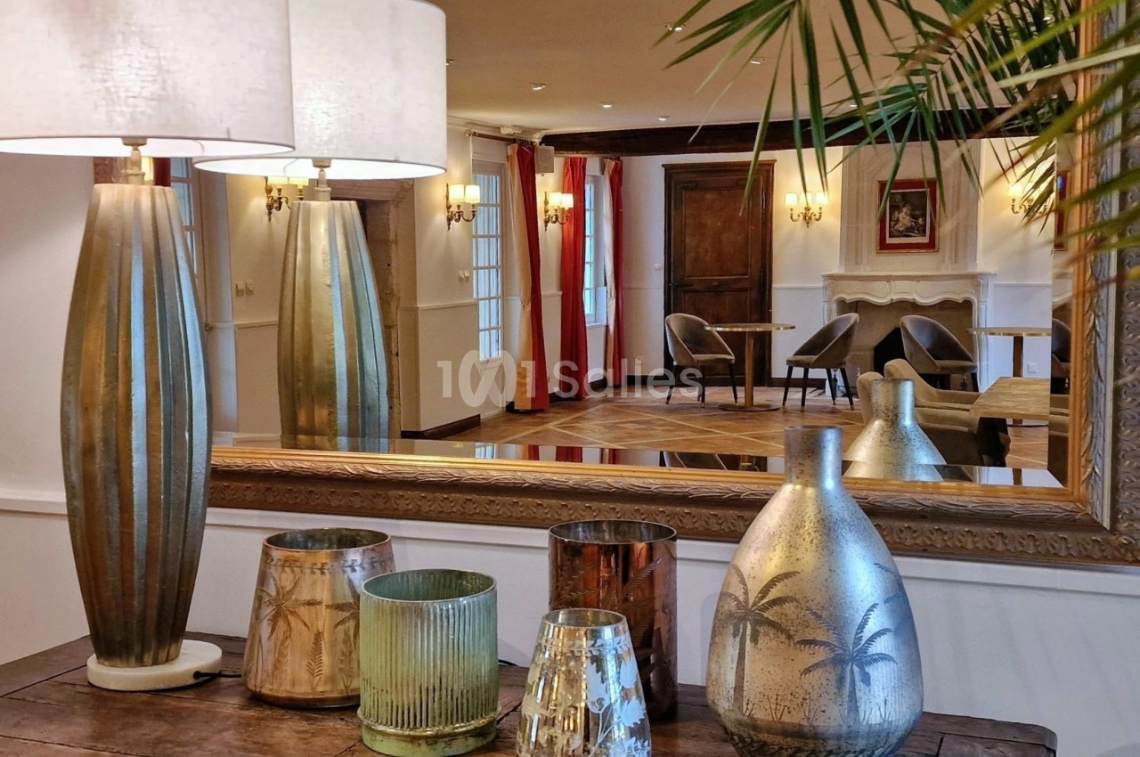 Lampes et vases décoratifs sur une table en bois, reflétés dans un grand miroir d'une pièce élégante et lumineuse.