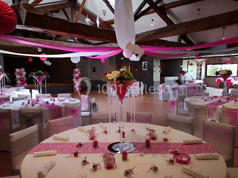 Salle de réception décorée avec des tons roses et blancs, tables dressées et ornées de centres de table fleuris.